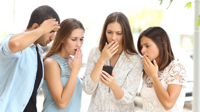 Four worried multi ethnic friends watching a smart phone in the street