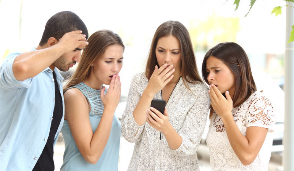 Four worried multi ethnic friends watching a smart phone in the street